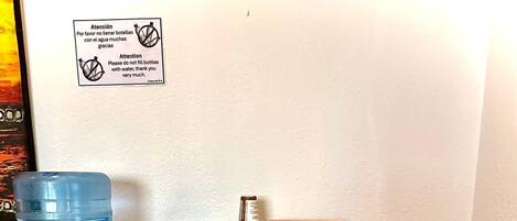 Une petite cuisine équipée d’un distributeur d’eau, d’une machine à café, d’un four à micro-ondes et d’une étagère avec des en-cas et un panier.