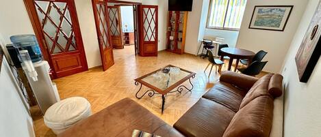 Een woonkamer met een bruine leren bank, een glazen salontafel en een televisie op een standaard.