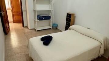 A small, clean room with a single bed, a white shelf unit, and a door leading to another room.