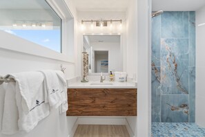 Une salle de bain avec un meuble-lavabo en bois, un lavabo blanc et une cabine de douche aux carreaux bleus.