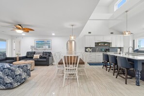 Une cuisine moderne avec des meubles blancs, un îlot central doté de tabourets et un ventilateur de plafond.
