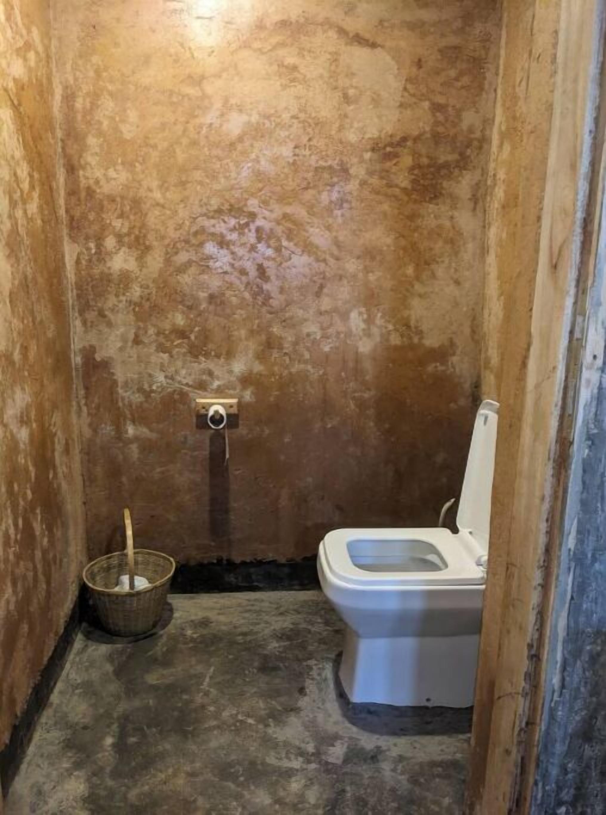 Ein kleines, abgeschlossenes Badezimmer mit Toilette und Eimer.