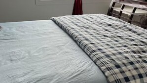 Una cama con sábana blanca y manta a cuadros.