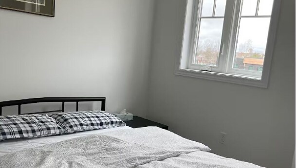 Un dormitorio con una cama, una ventana y una lámpara fijada a la pared.