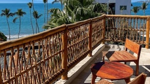 Ein Balkon mit Holzmöbeln, Blick auf das Meer und ein Gebäude mit Satellitenschüsseln.
