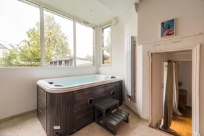 A room with a hot tub, a window, and a door leading to another room.