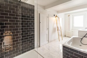 A modern bathroom with a black and white tiled wall, a white bathtub, and a wooden ladder.