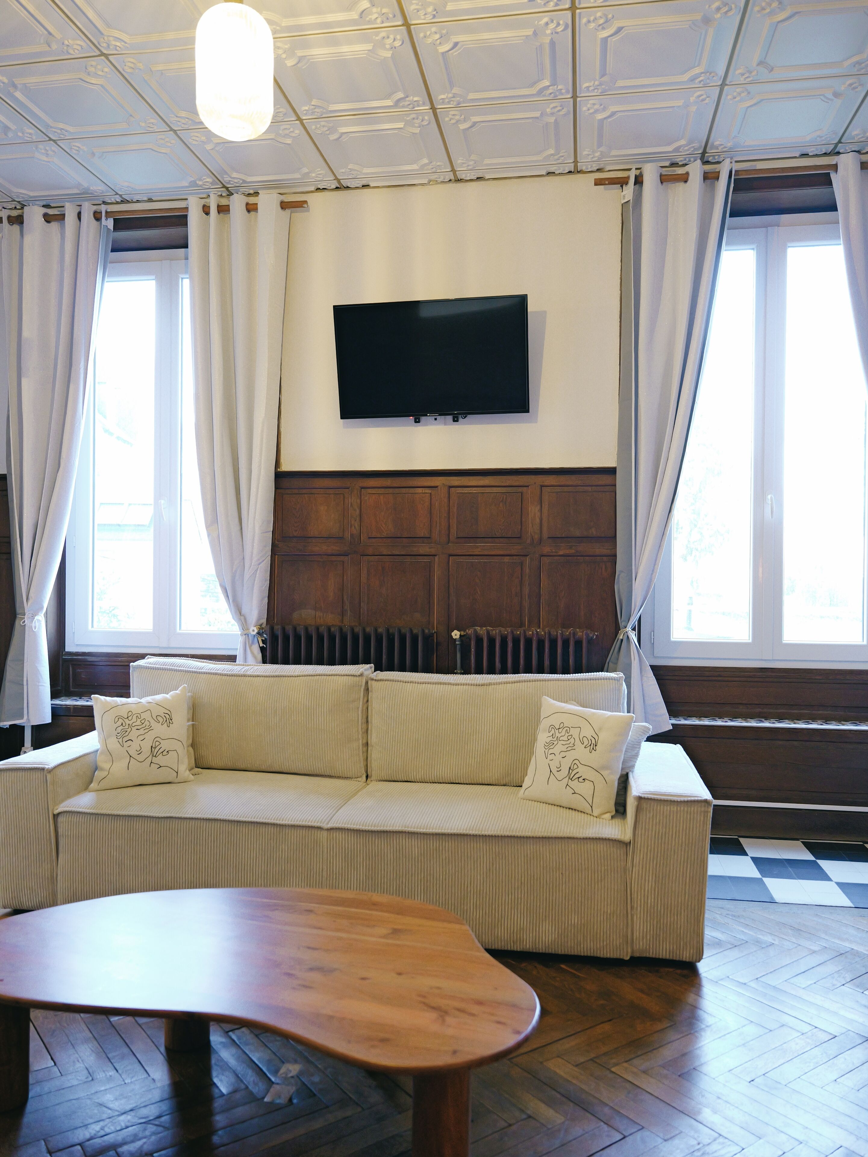 A living room with a sofa, a wooden coffee table, a flat-screen TV mounted on the wall, and a radiator below.