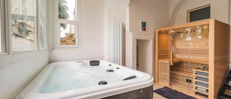 A spa room with a hot tub, wooden sauna, and a view of the outside.