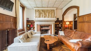 A cozy living room with a fireplace, a sofa, a coffee table, and a television mounted on the wall. - La Royale Jacuzzi Sauna Jardin Gare - Hôtel Lefort (Guingamp)