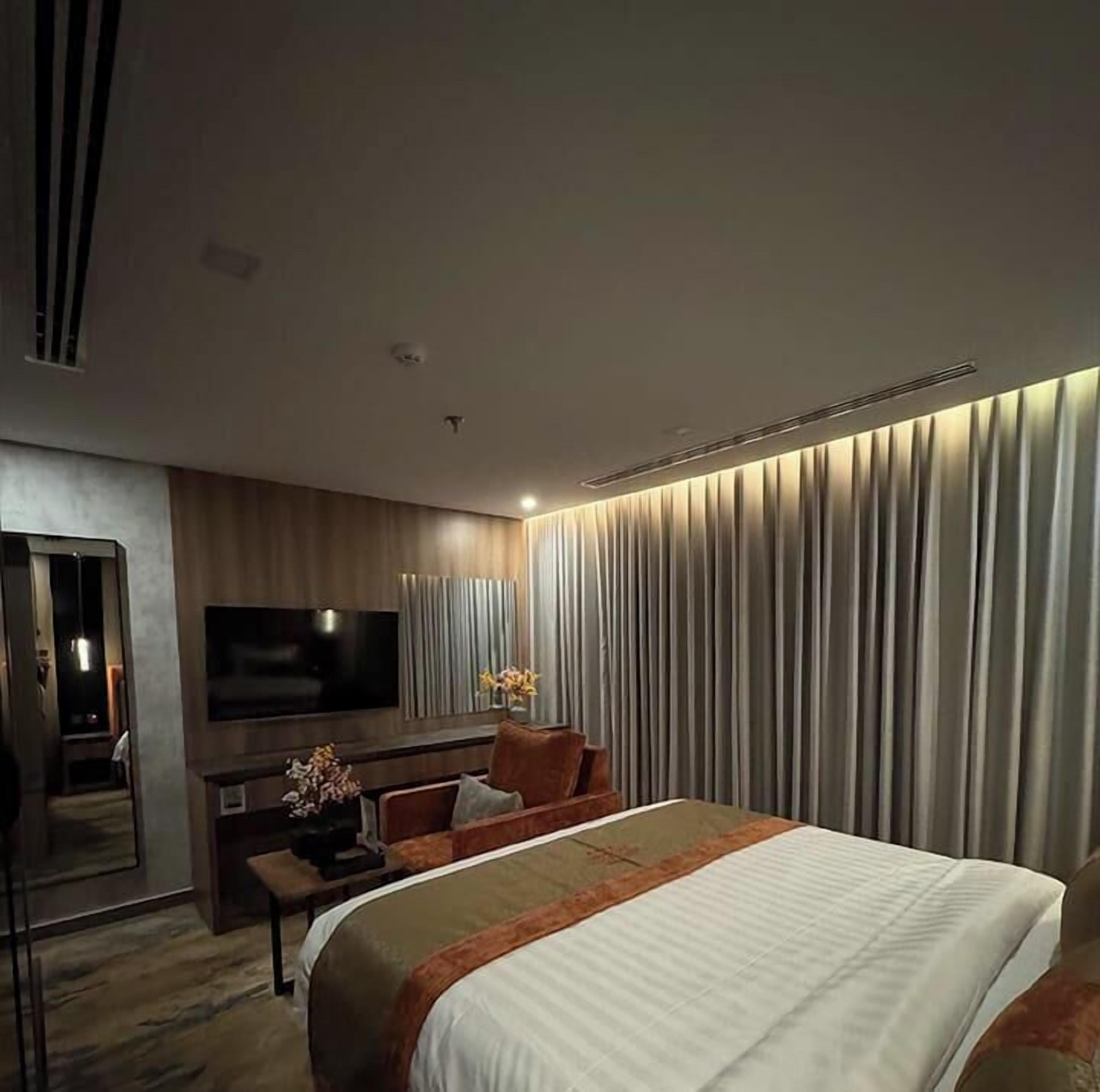 A modern hotel room with a large bed, a flat-screen TV, a desk, and a seating area.