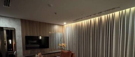 A modern hotel room with a large bed, a flat-screen TV, a desk, and a seating area.