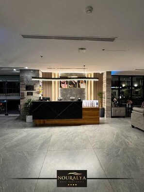 Un área de recepción moderna de hotel con un mostrador de mármol, un panel de madera decorativo y un amplio ventanal.