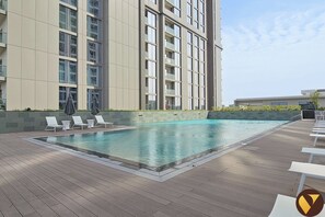 A modern building with a swimming pool, lounge chairs, and a tiled deck.