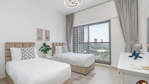 A modern hotel room with two beds, a large window with a city view, a desk with a lamp, and a plant on the nightstand. - Brand New with Relaxing Pool & Kids Area (Dubai)