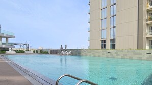 A modern building with a rooftop pool area, including lounge chairs and a clear view of the city skyline. - Brand New with Relaxing Pool & Kids Area (Dubai)