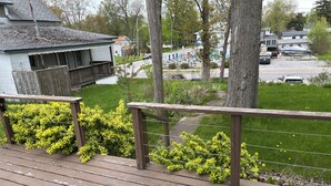 A wooden deck with a railing, surrounded by green shrubs and a grassy area.