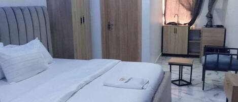 A hotel room with a bed, a wooden wardrobe, a desk with a chair, and a small table.