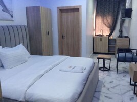 Habitación de hotel con una cama, un armario de madera, un escritorio con una silla y una mesita.