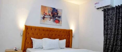 Habitación de hotel con una tapizada naranja, ropa de cama blanca, un cuadro en la pared y una cortina negra.
