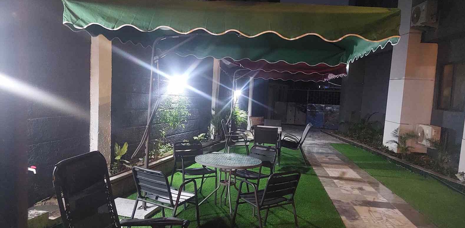 An outdoor patio with a round table and chairs, a green awning, and a pathway leading to a building.