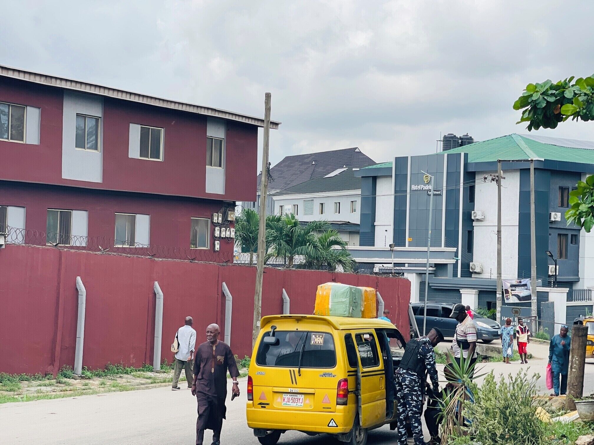 A yellow van parked on a street with a red building and a hotel in the background.