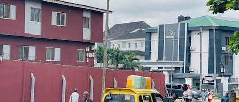 A yellow van parked on a street with a red building and a hotel in the background.