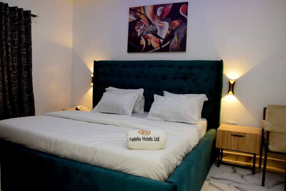 En snyggt bäddad säng med vita sängkläder och en kudde med logotypen för Padelia Hotels Ltd.