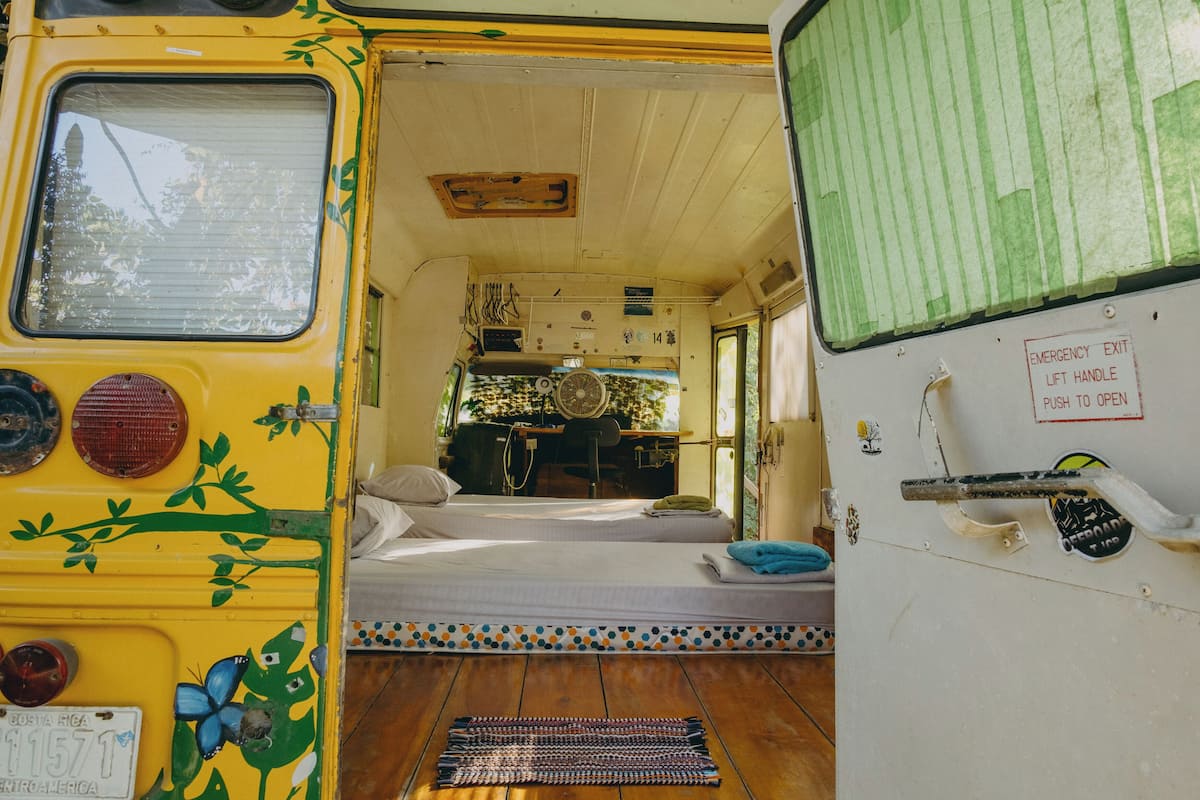 A compact, well-lit interior with a bed, a small table, and a fan.