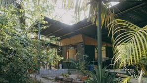 A covered outdoor area with a gravel path, surrounded by various plants and a building with a metal roof. - Chilamate Rainforest Beach Retreat (Nosara)