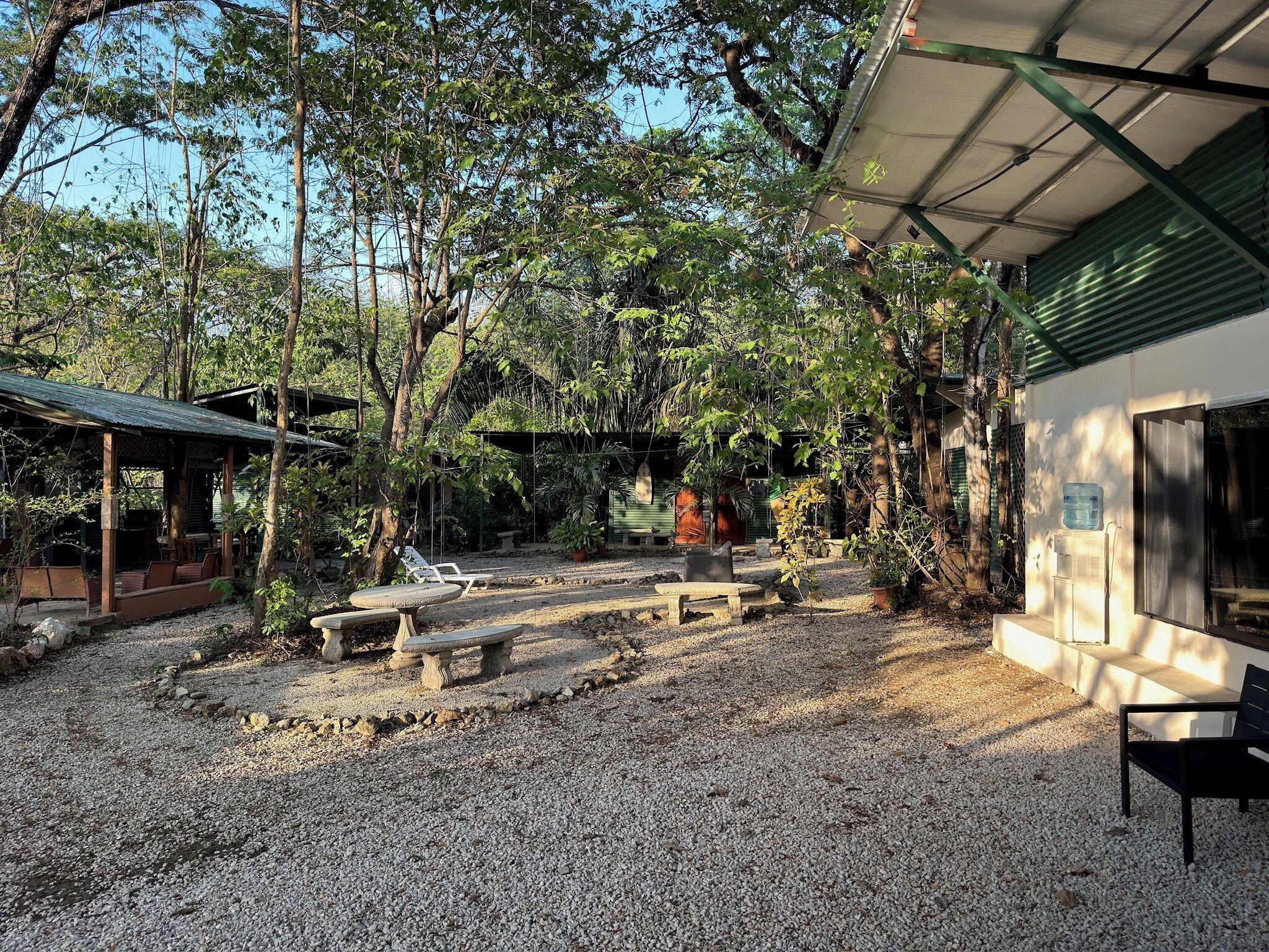 A covered outdoor area with seating, a water dispenser, and a building with a green roof.