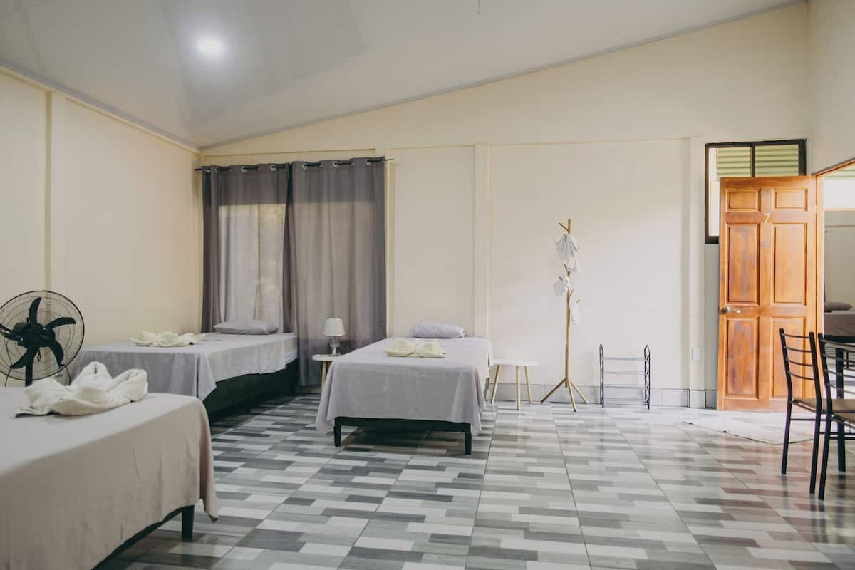 A hotel room with two beds, a fan, a lamp, and a wooden door.