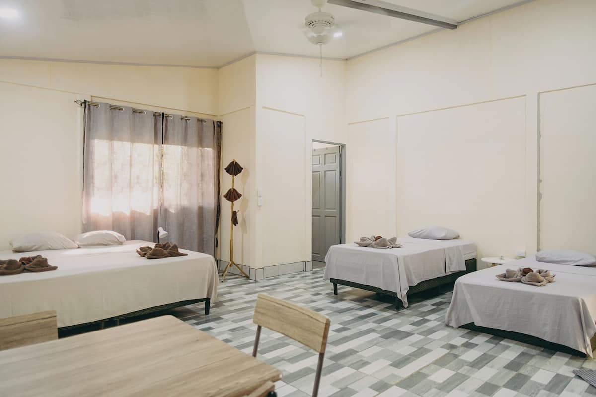 A hotel room with two beds, a desk, a chair, a floor lamp, and a door.