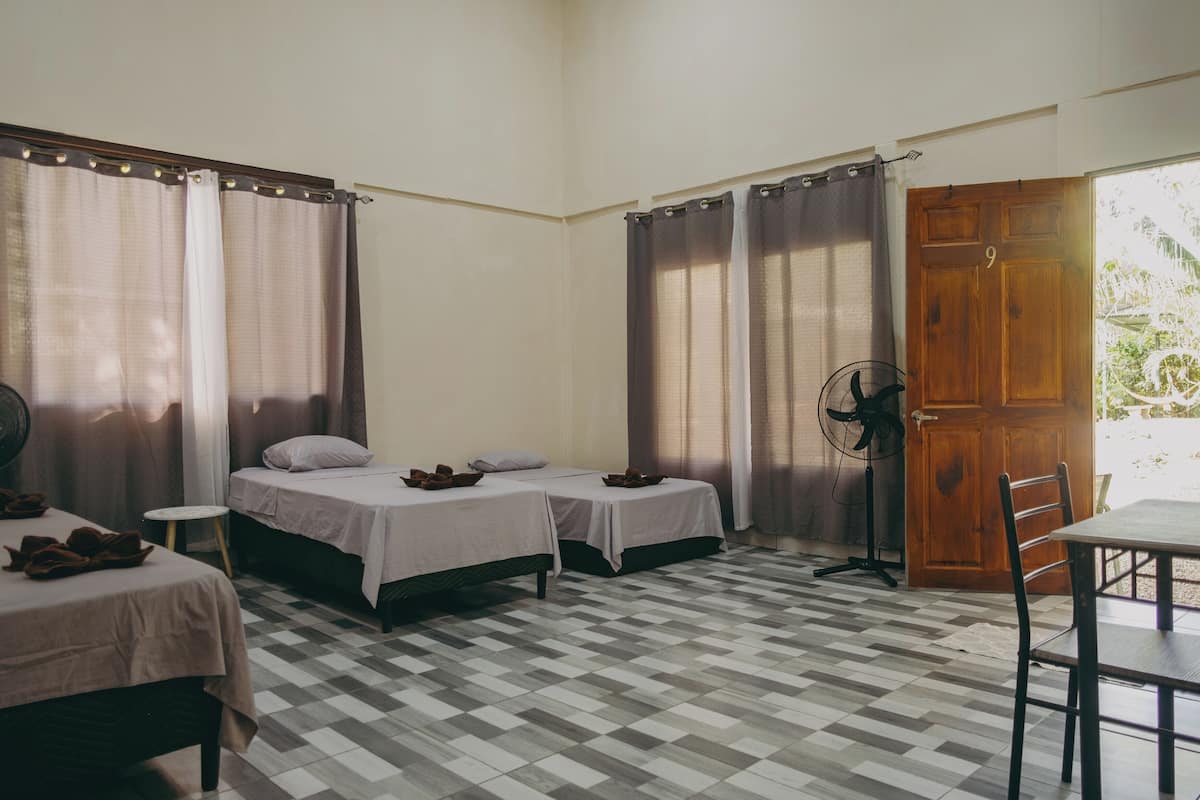 A room with two single beds, a small round table, a fan, and a wooden door.
