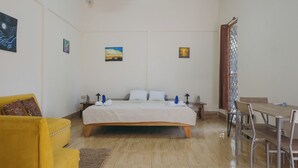 A bedroom with a bed, a yellow armchair, a dining table with chairs, and artwork on the walls. - Chilamate Rainforest Beach Retreat (Nosara)