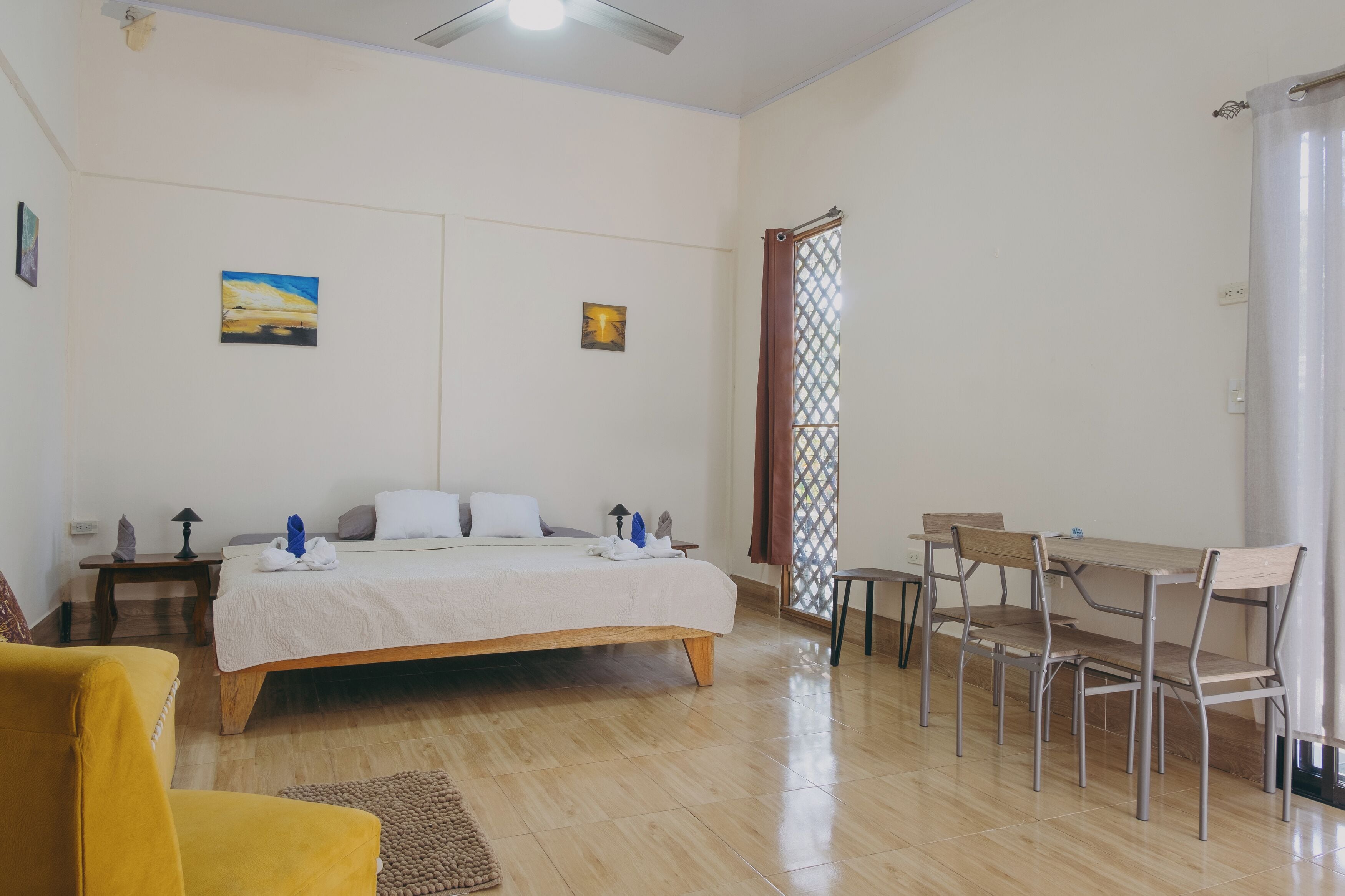 A bedroom with a bed, bedside tables, a desk with chairs, and a window with a curtain.