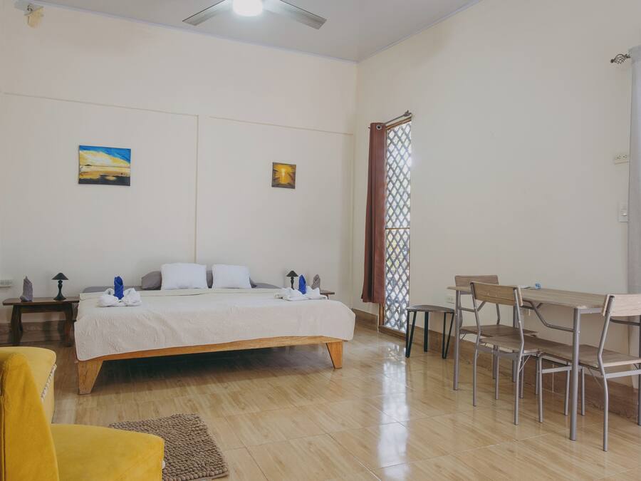 A bedroom with a bed, bedside tables, a desk with chairs, and a window with a curtain.