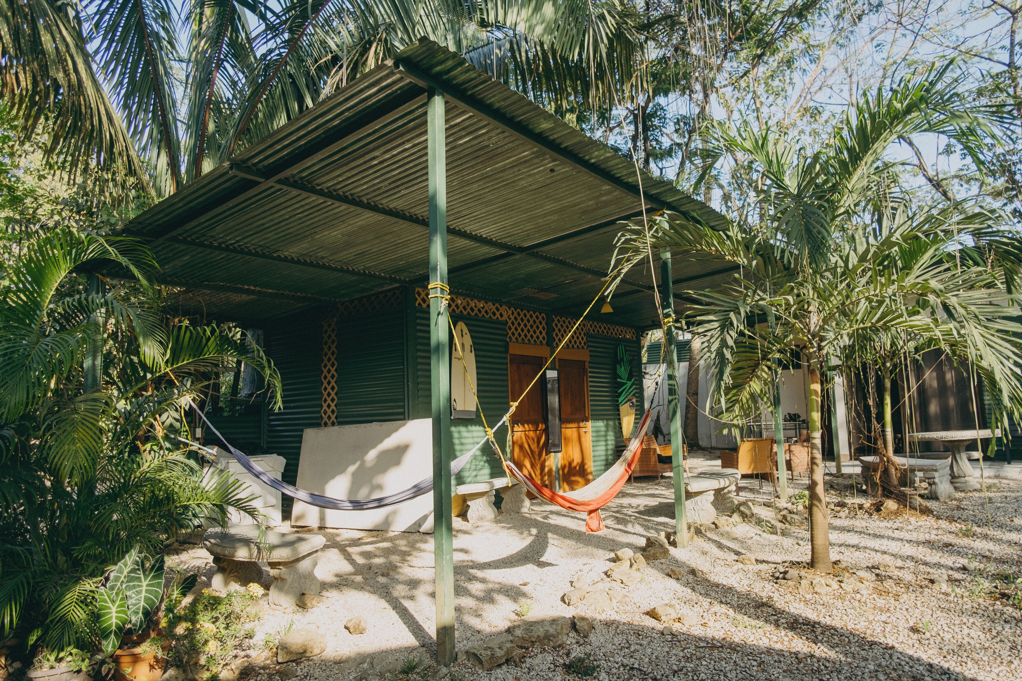 Una casa rústica con una hamaca, palmeras y un porche cubierto.