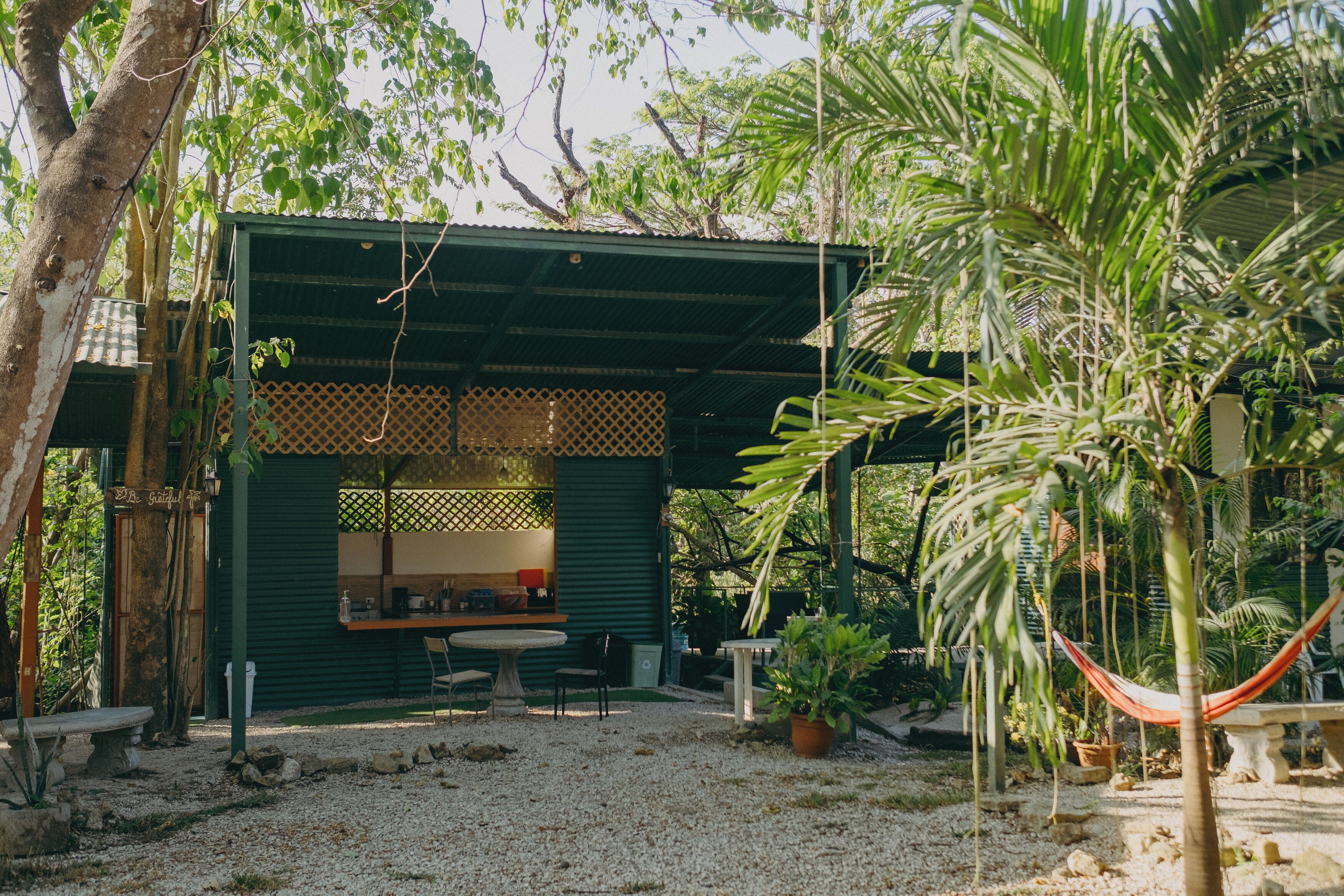 Un espace extérieur aménagé avec une table et des chaises, protégé par un auvent et entouré de verdure, avec un hamac à proximité.