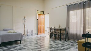 A room with a bed, a dining table with chairs, a small table with a statue, and a window with curtains. - Chilamate Rainforest Beach Retreat (Nosara)