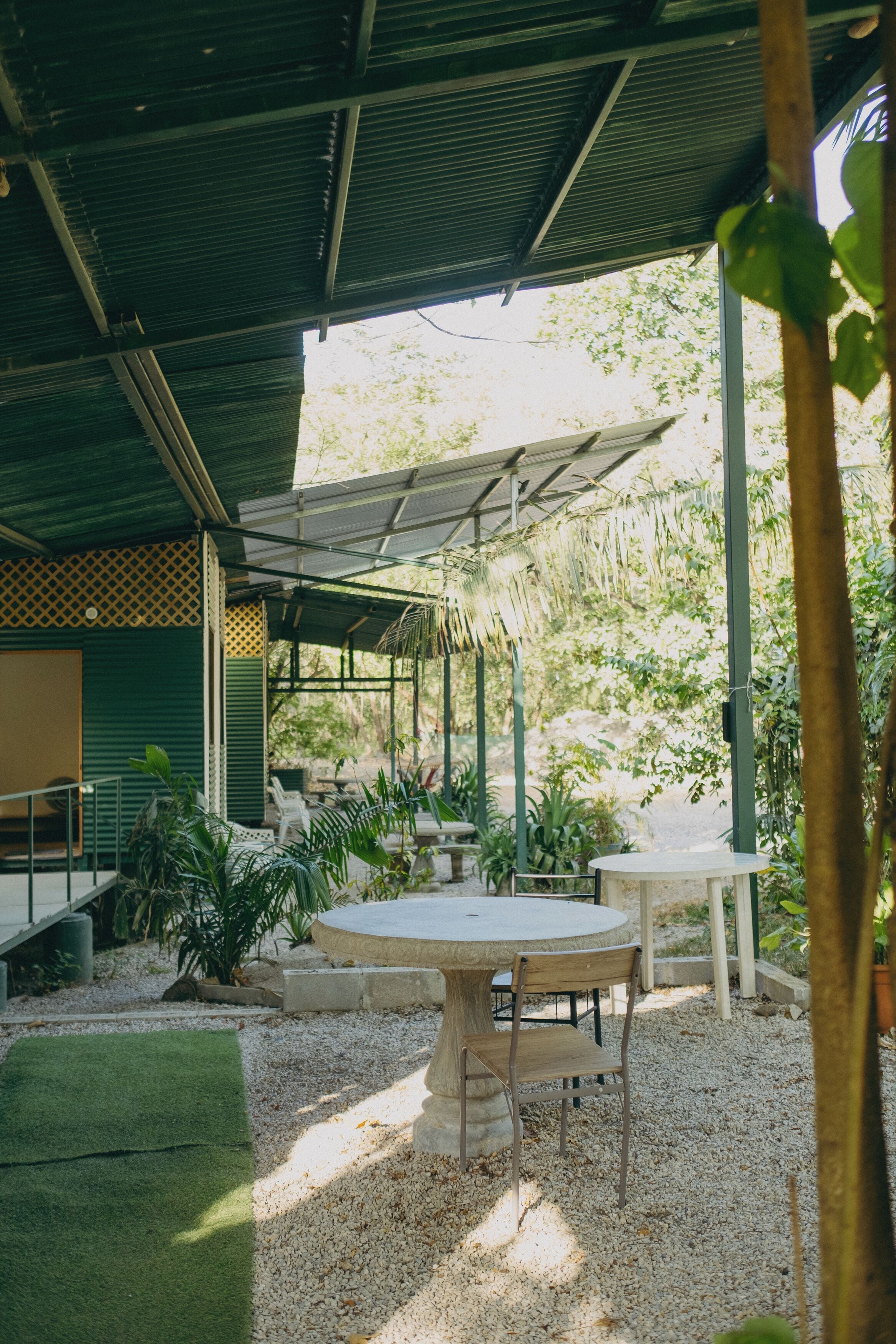 An outdoor patio area with a round table and chairs, surrounded by plants and a covered seating area.