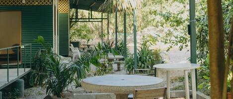 An outdoor patio area with a round table and chairs, surrounded by plants and a covered seating area.