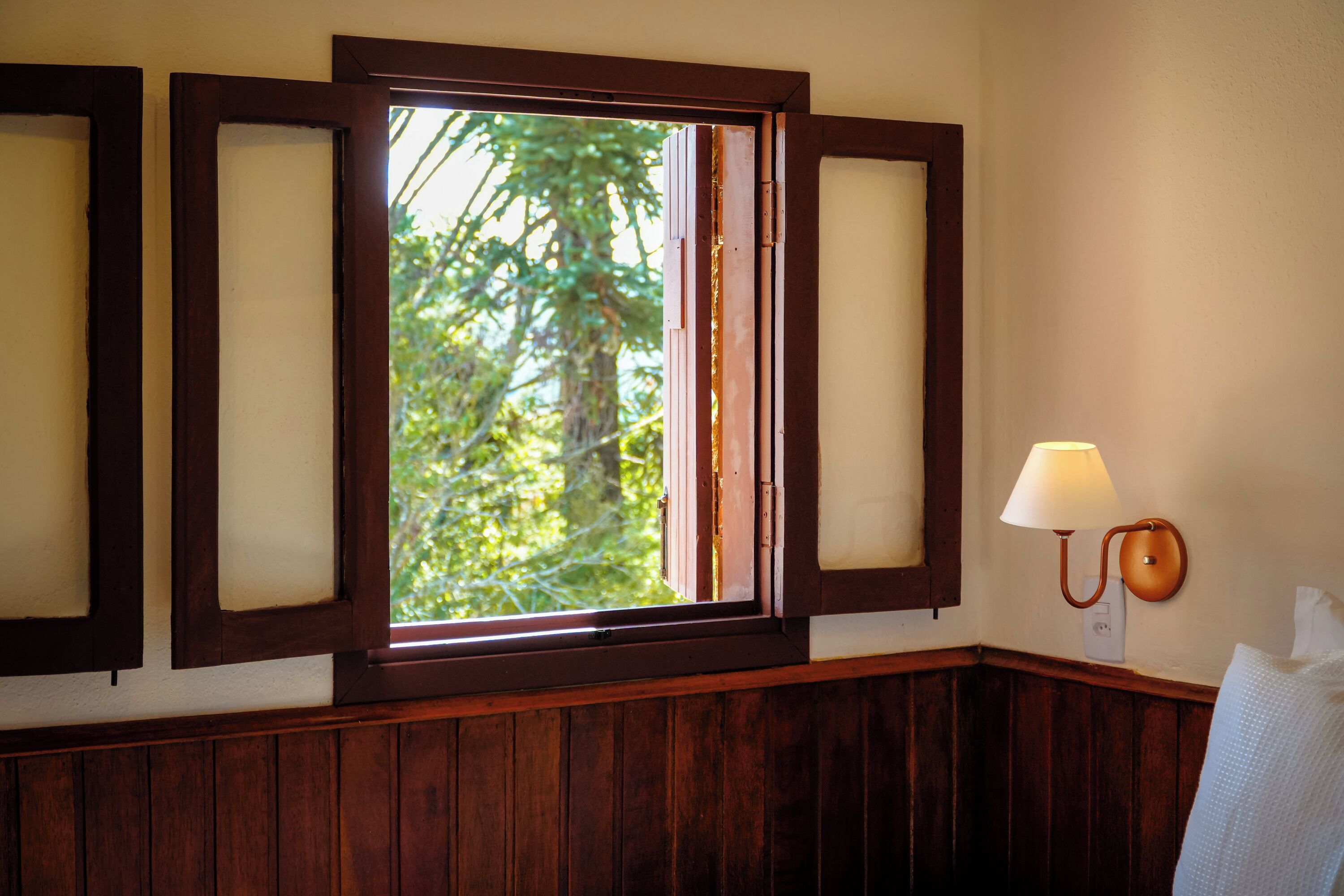 A room with a large window, wooden paneling, and a wall-mounted lamp.