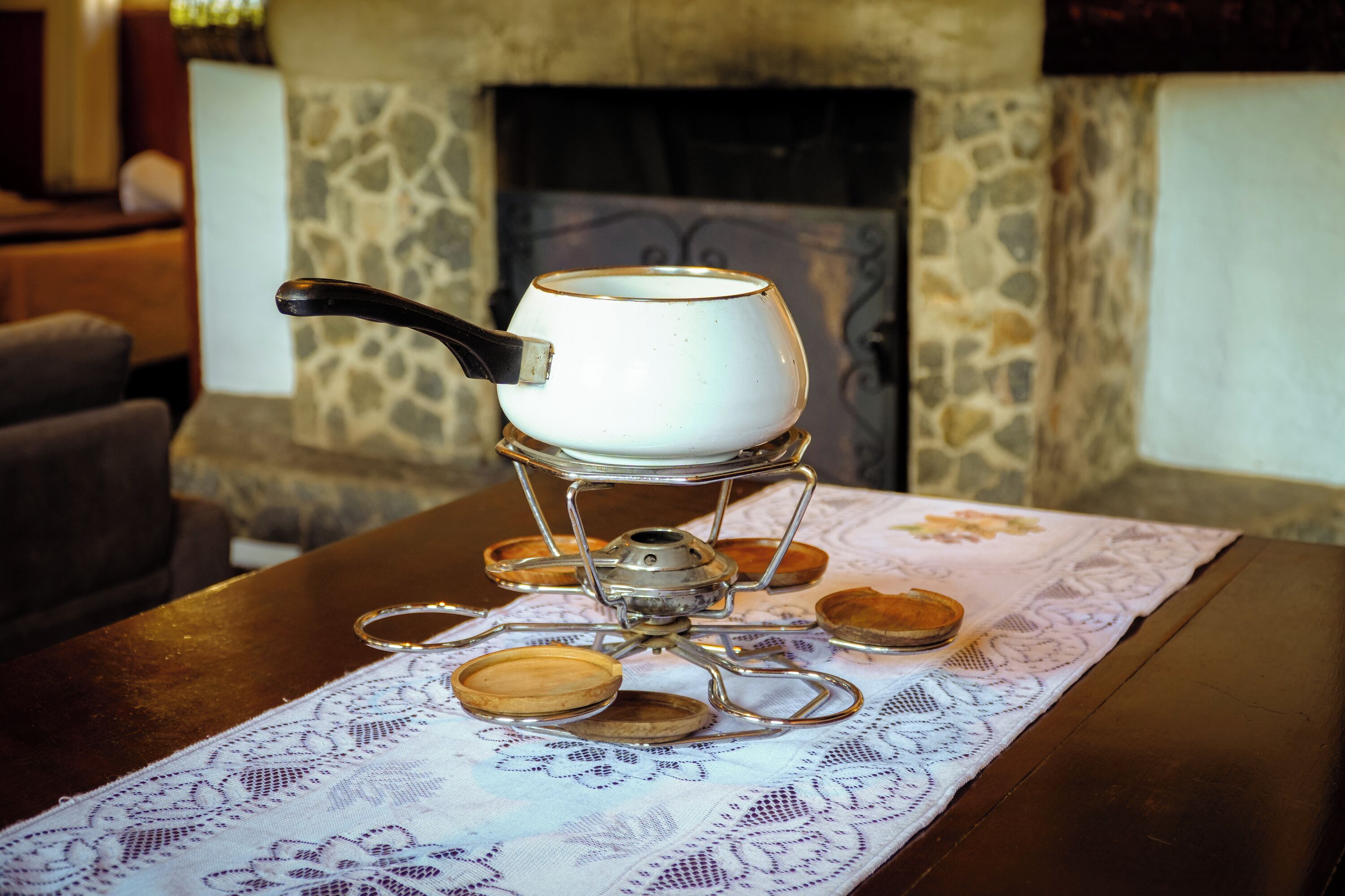A traditional tea set on a lace tablecloth with a stone fireplace in the background.