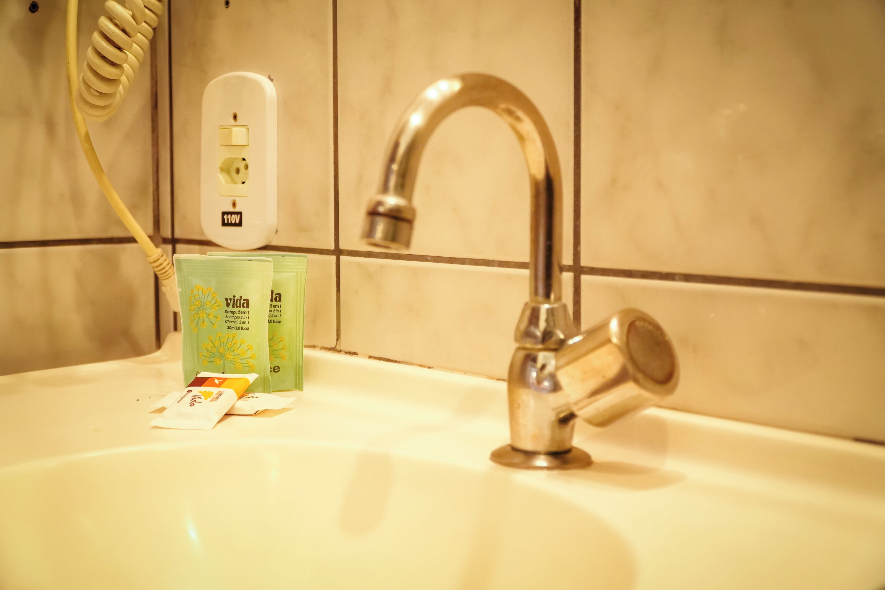 A bathroom sink with a faucet, a power outlet, and toiletries.