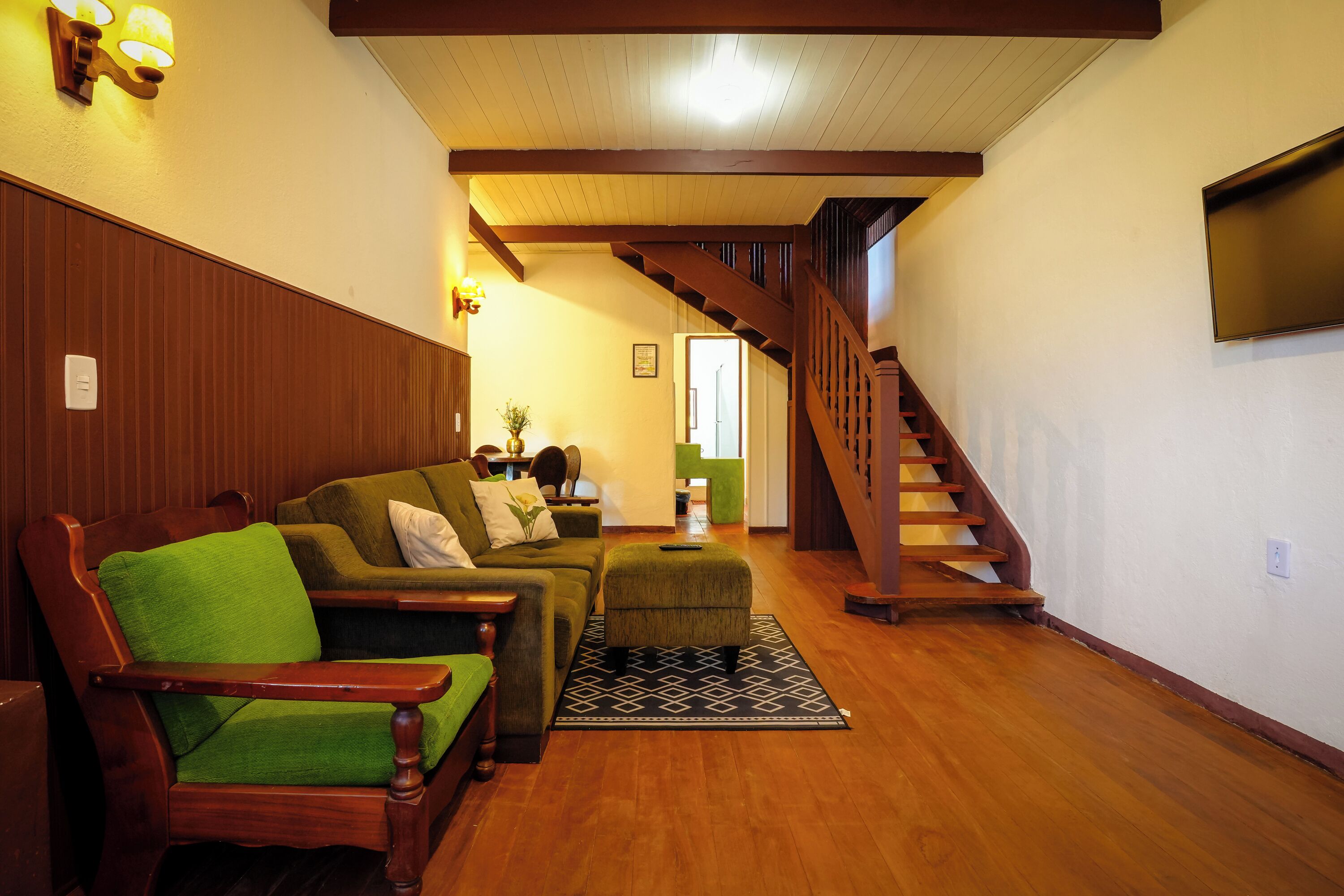 Una sala de estar con una escalera de madera, sofás tapizados en verde y un rug con estampado blanco y negro.