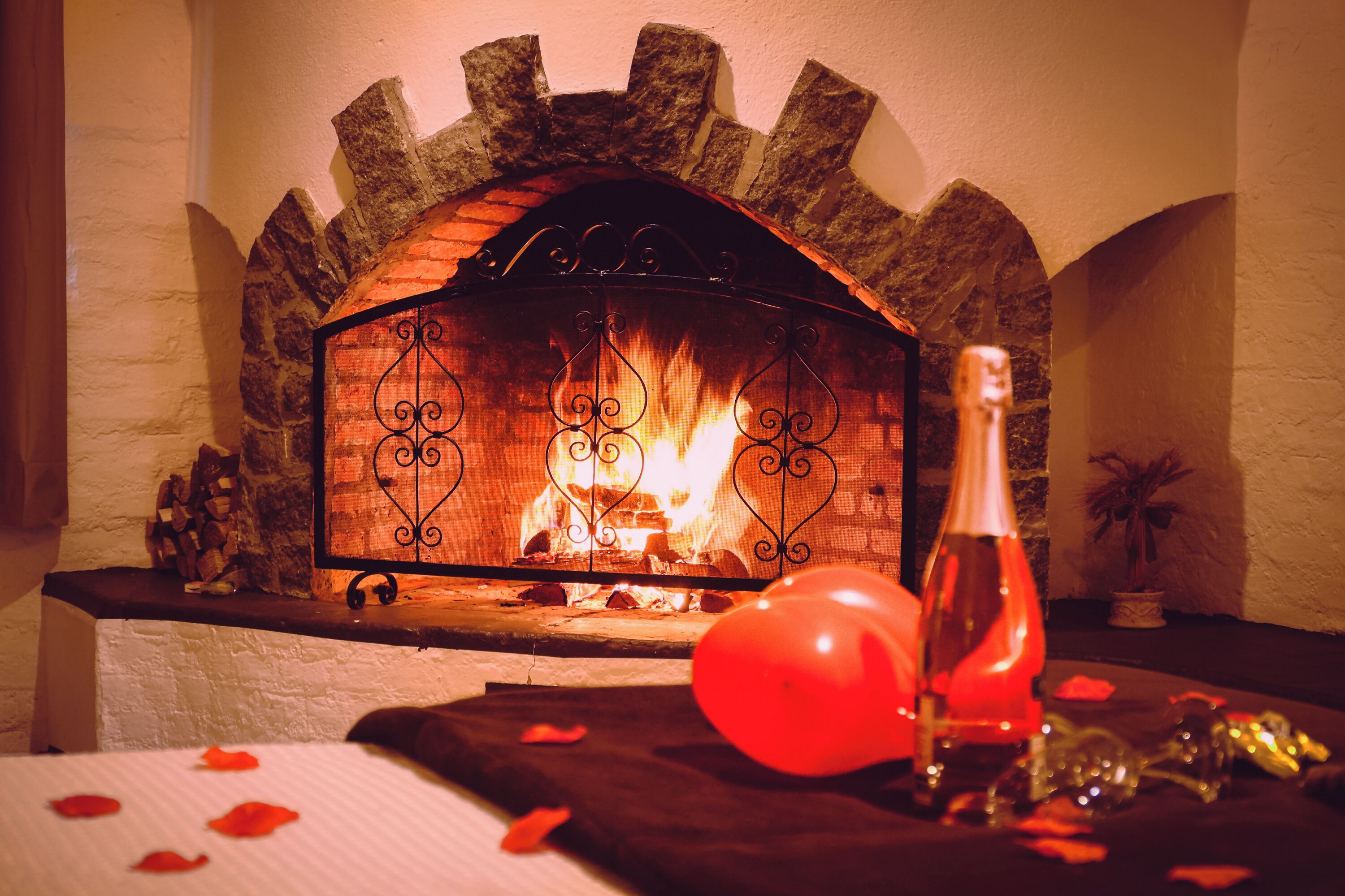Una chimenea con arco de piedra, una botella y globos sobre una mesa.