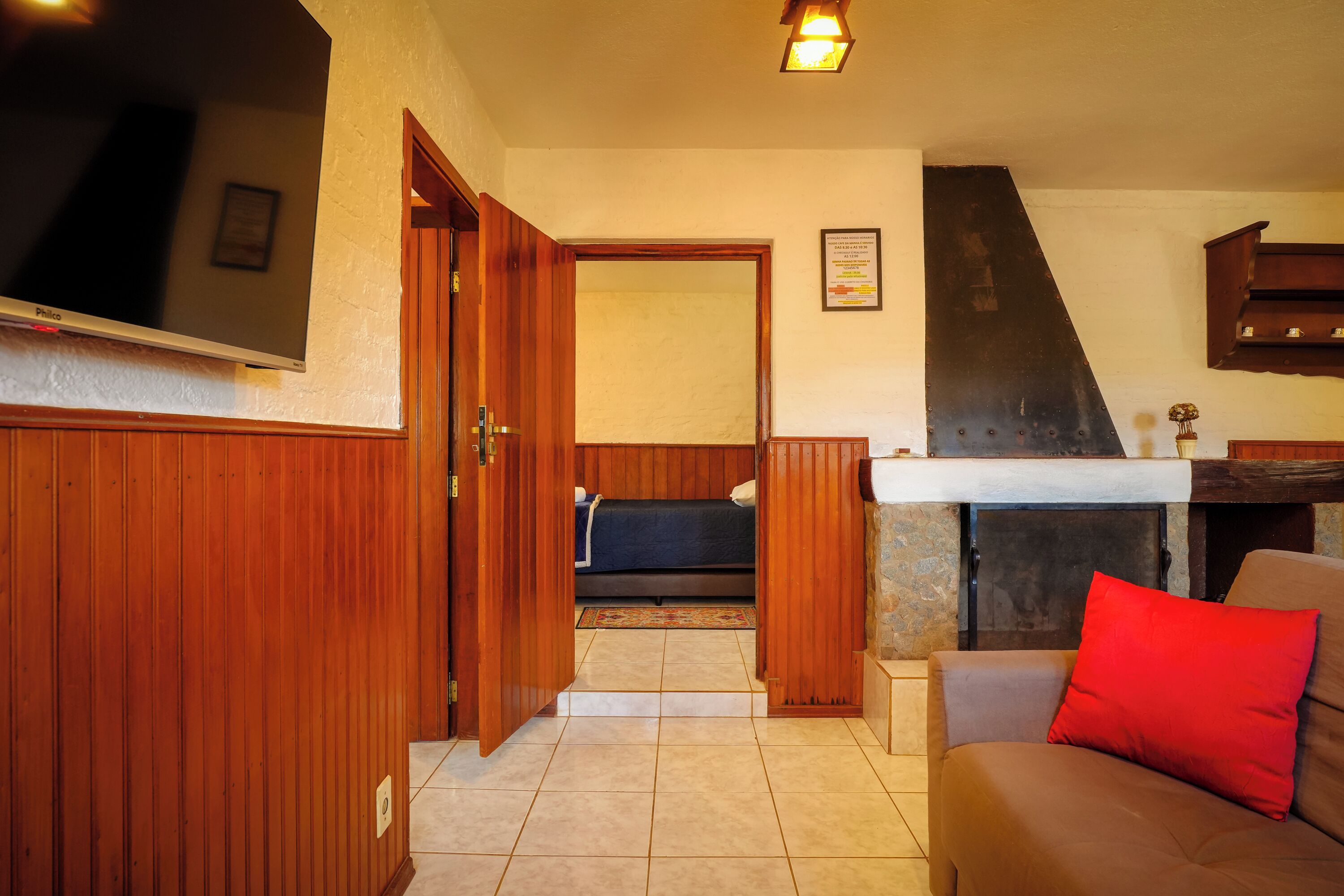 Una sala de estar acogedora con una televisión de pantalla plana, paredes de madera, una chimenea y un sofá con un cojín rojo.