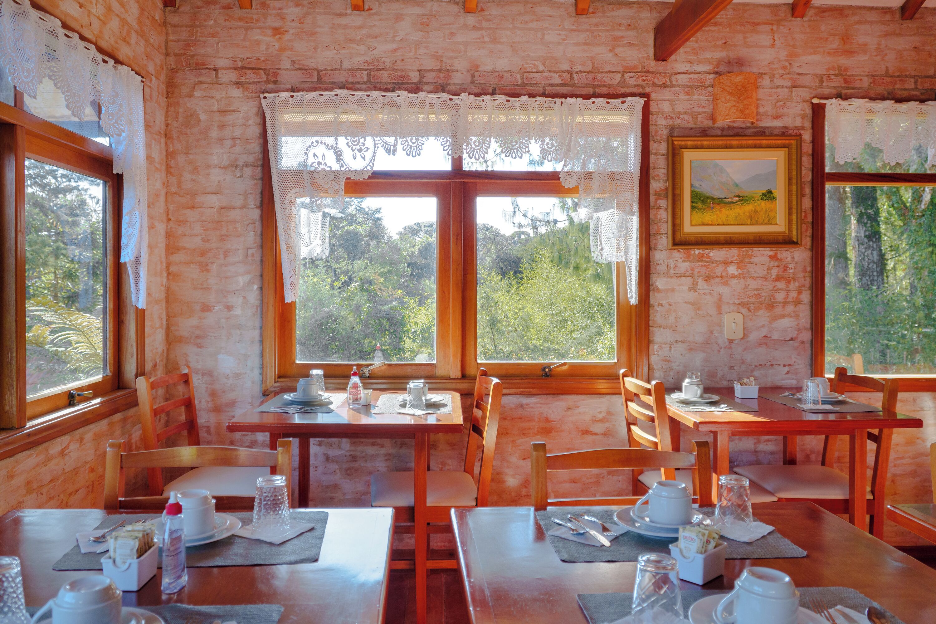 Uma sala de jantar com mesas e cadeiras de madeira, cortinas de renda e um quadro na parede.