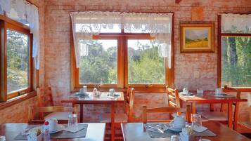 Uma sala de jantar com mesas e cadeiras de madeira, cortinas de renda e um quadro na parede.